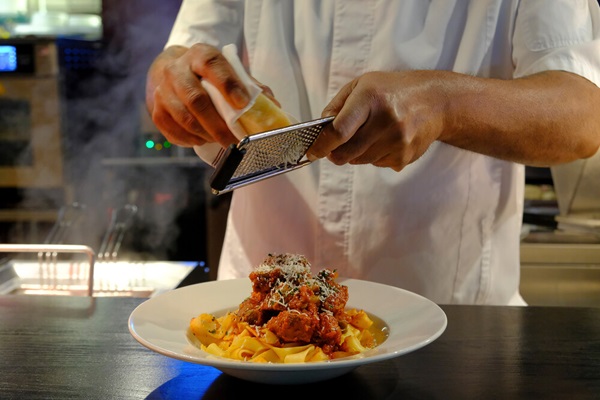 A chef grating parmesan cheese onto pasta