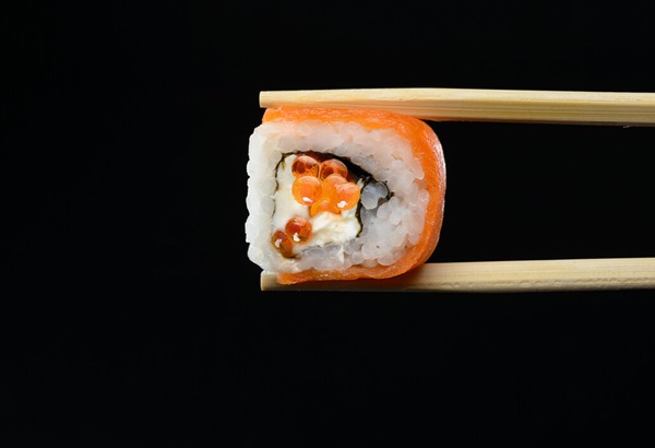 close shot of sushi roll being held by chop sticks